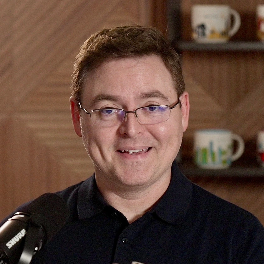 Brian smiling in his studio, with travel mugs on the shelves behind him
