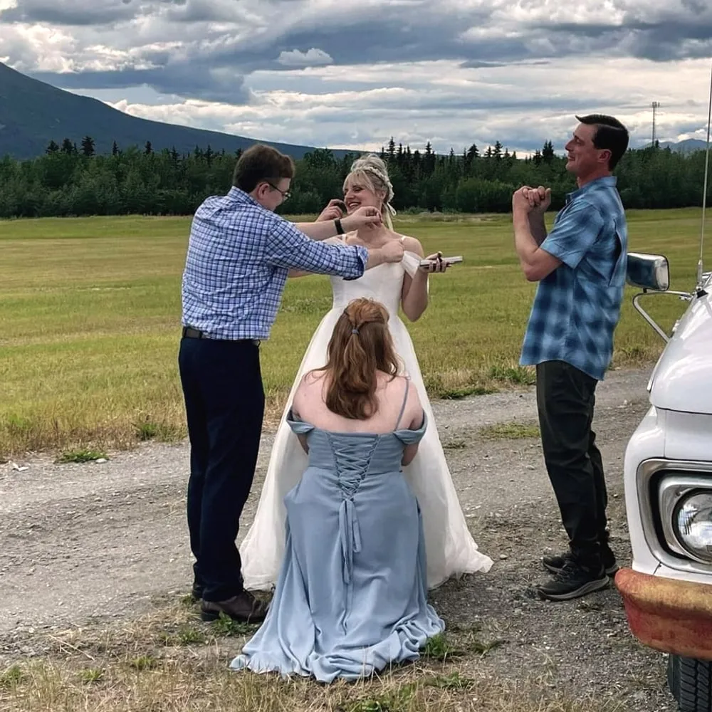 Brian putting a mic on Ellyn before her ceremony in an open field in Alaska, mountains and storm clouds behind