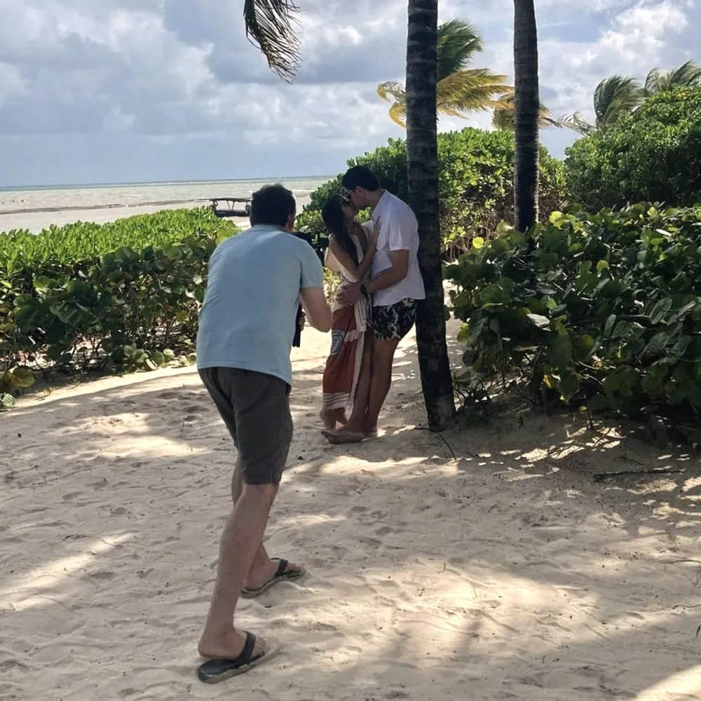 Brian filming Tonya and Ori kissing under the palm trees on the beach in Tulum, Mexico, at their destination wedding