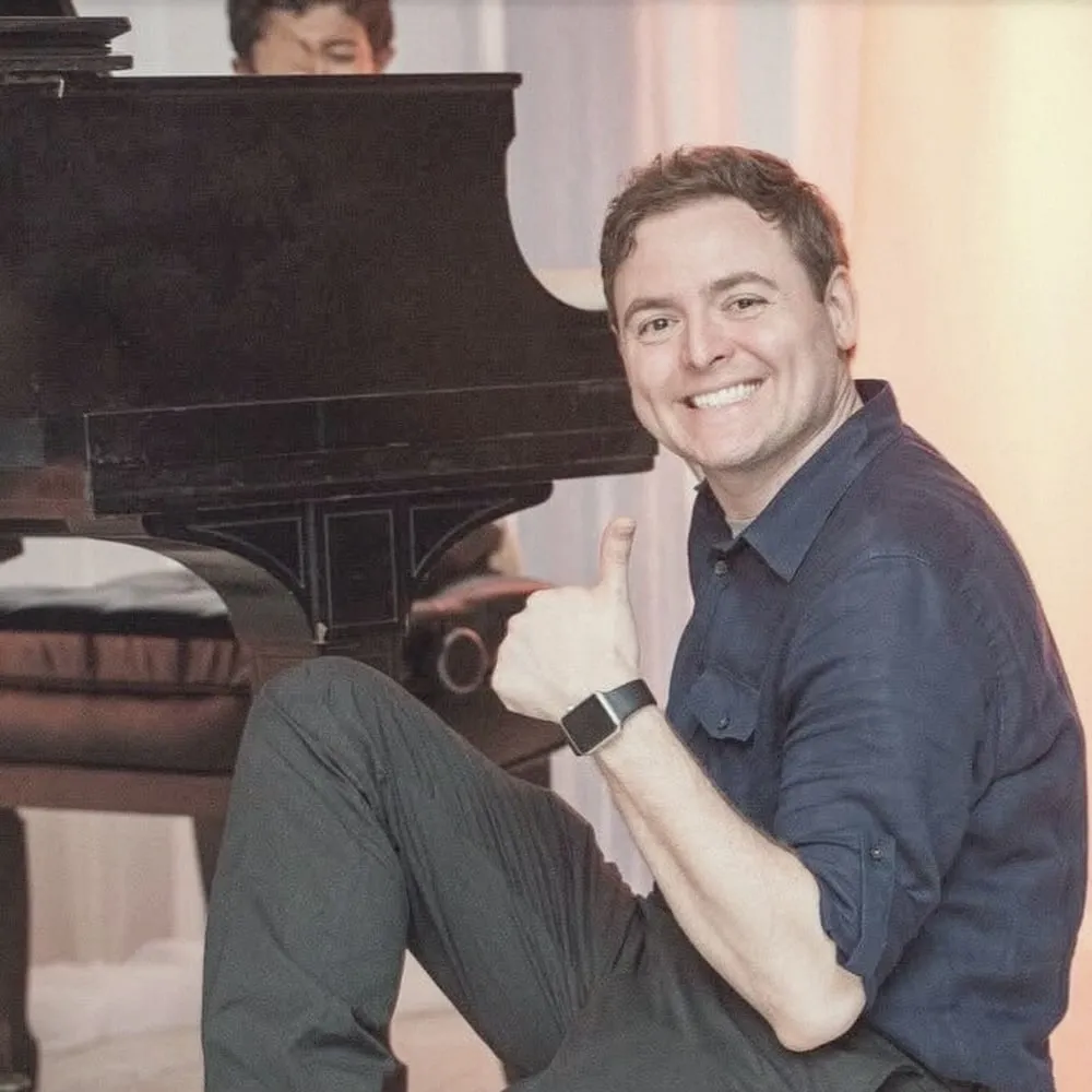 Brian on the floor beside a grand piano during the reception speeches, giving a thumbs up while holding the key cover shut