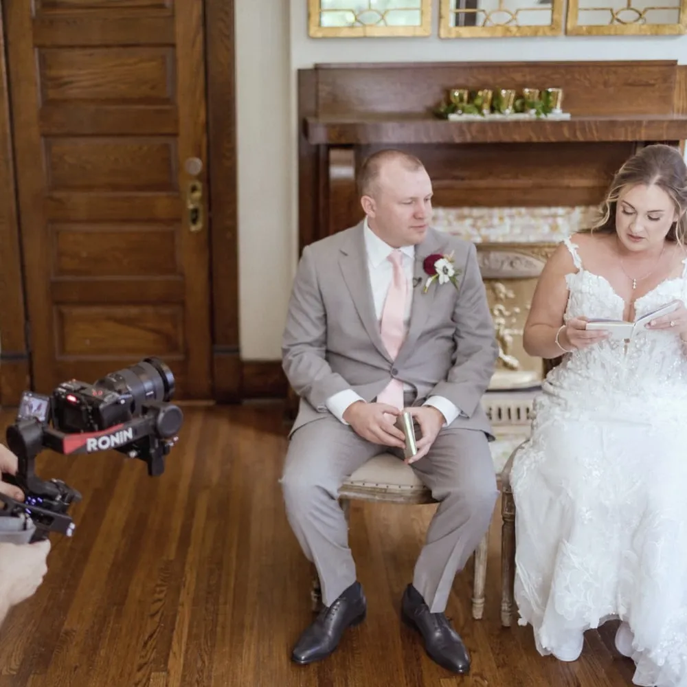 Nicole and Jeff seated side by side at CJ's Off the Square as Nicole reads her private vows from a small book, Brian's camera rig in the foreground