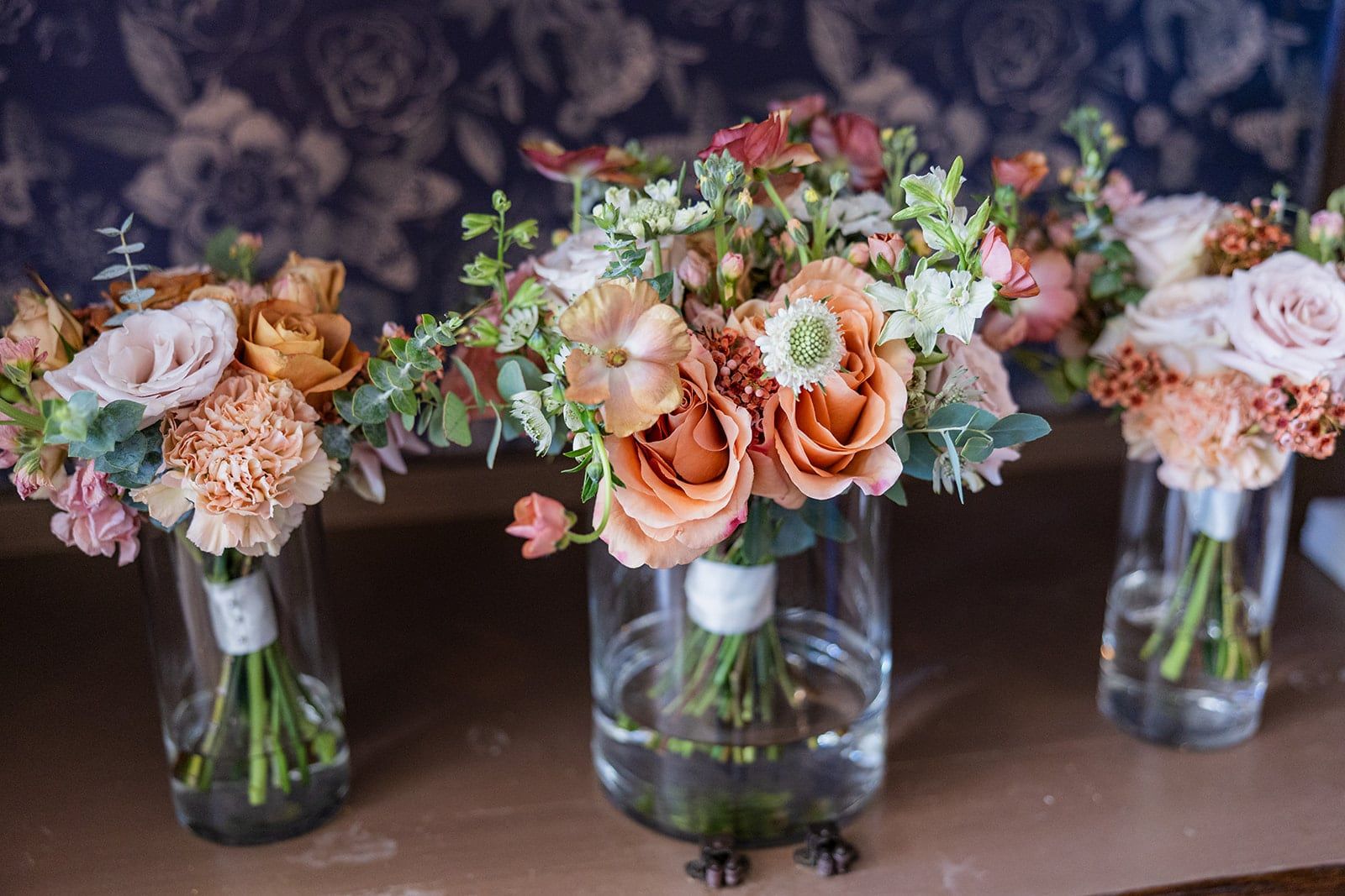 Bouquets of peach roses, ranunculus and blue delphinium waiting in glass vases