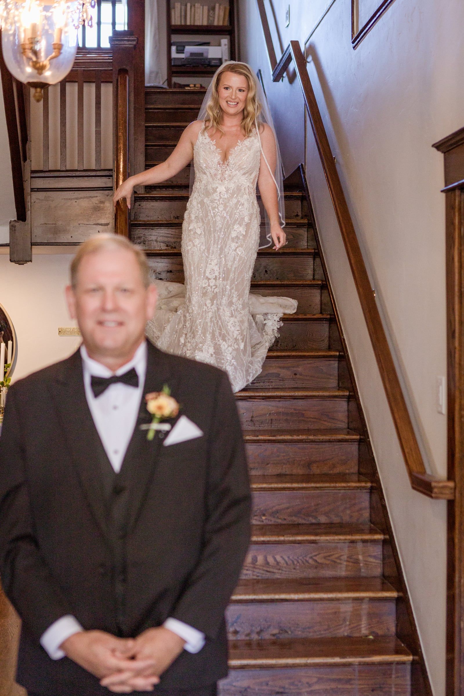 First look with her dad: Caitlin walks down the wooden staircase as her dad waits at the bottom, smiling
