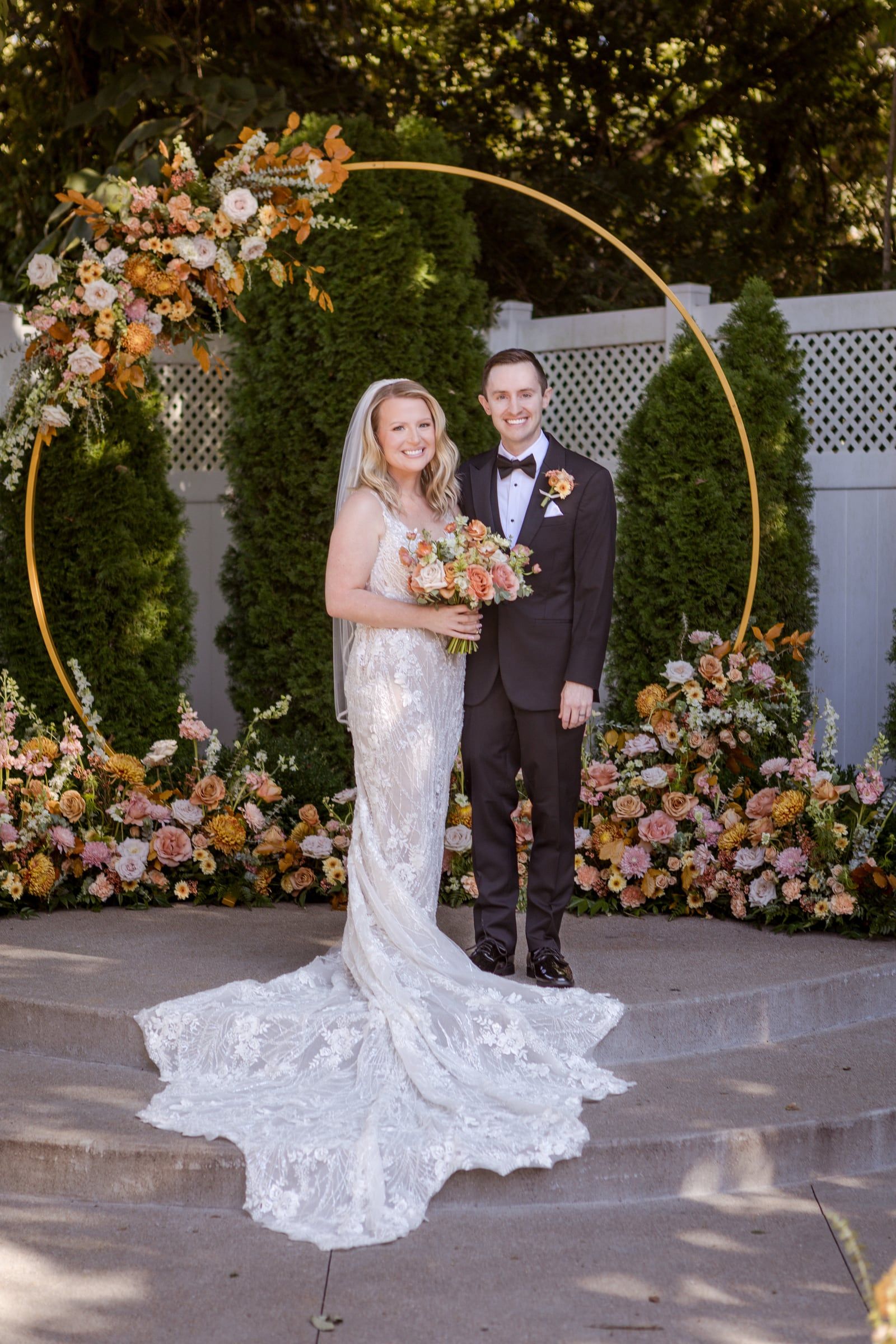 Caitlin and Gunnar stand together in front of the floral ceremony arch