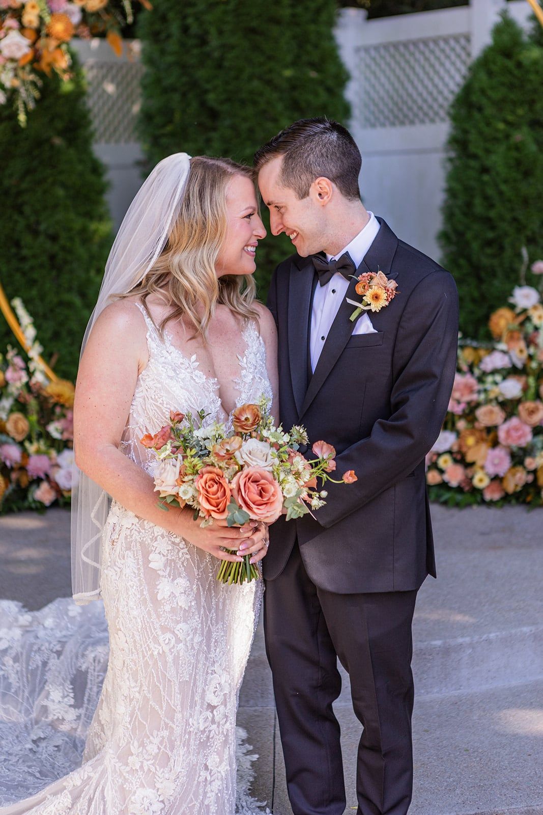 Caitlin and Gunnar touch foreheads and smile, her peach bouquet between them