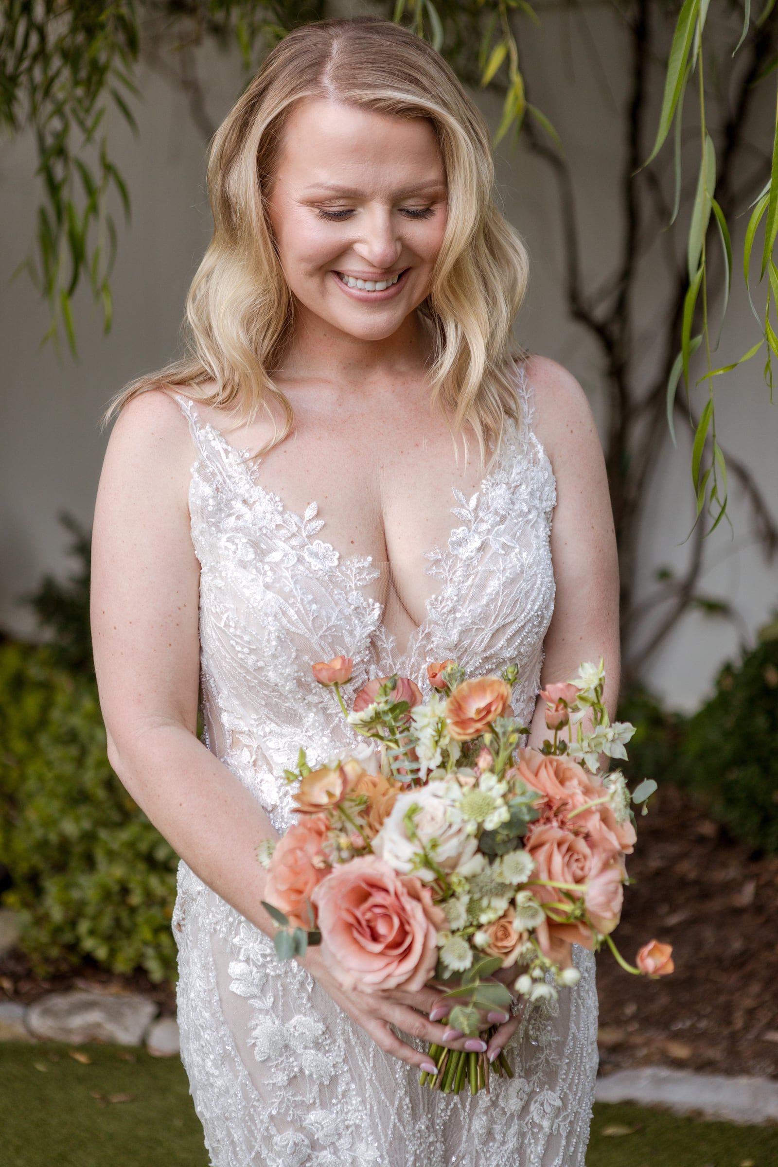 Caitlin looks down at her bouquet and laughs in the garden