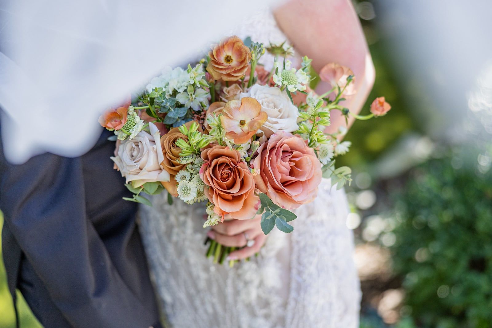 Close-up of Caitlin's bouquet of peach roses and ranunculus against her lace gown
