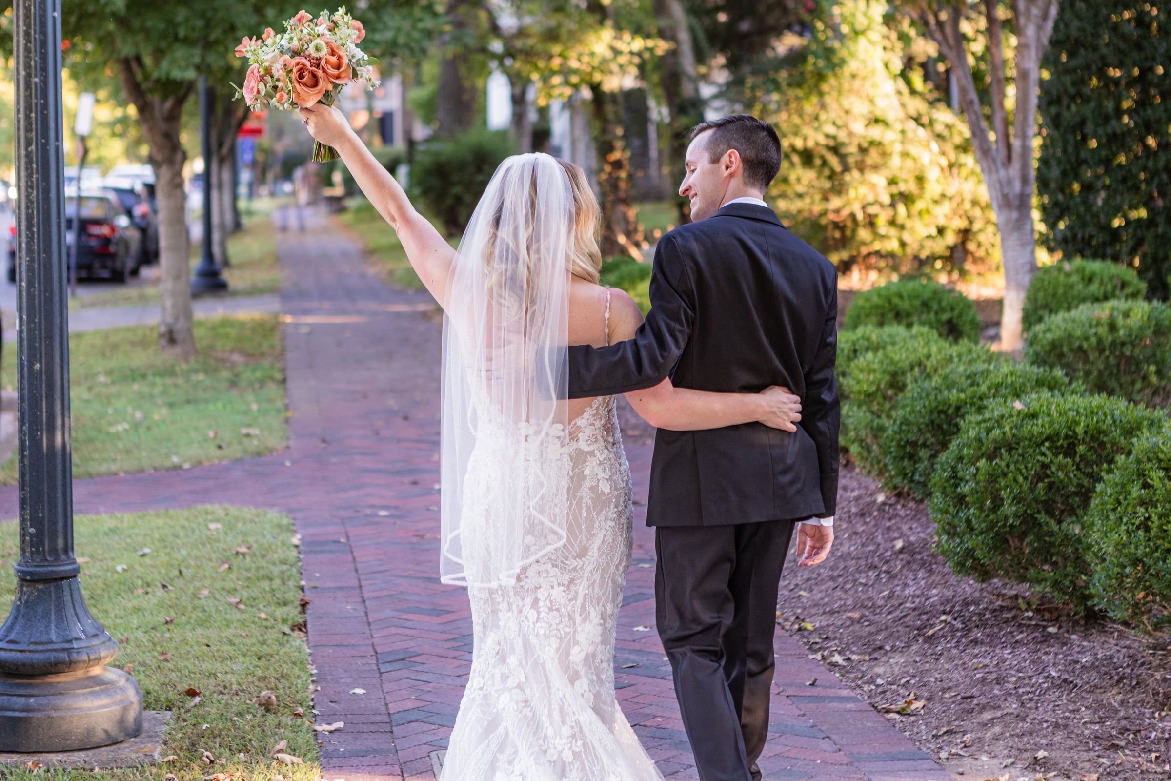 Caitlin raises her bouquet in celebration as she and Gunnar walk down the sidewalk
