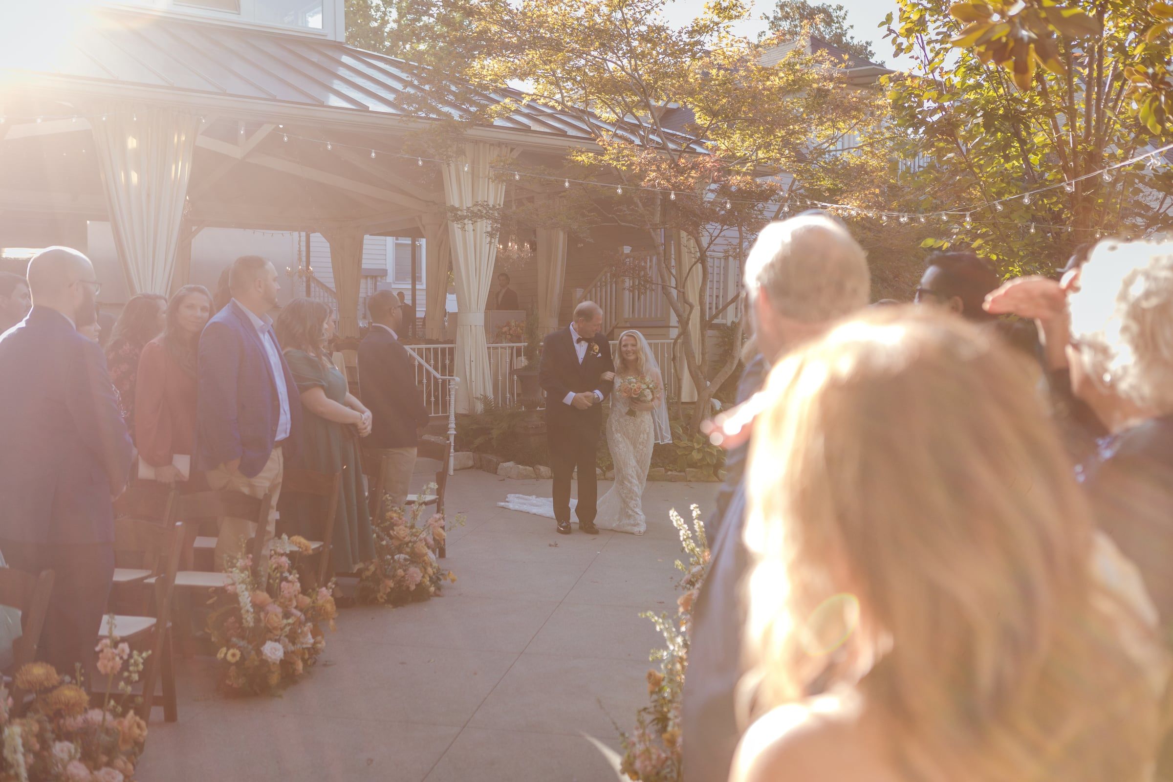 Sunlit view down the garden aisle as guests turn to watch the processional