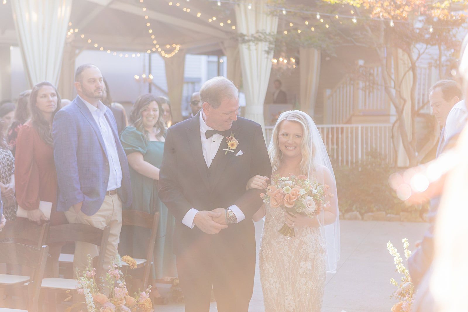 Caitlin's dad walks her down the aisle as guests stand and smile