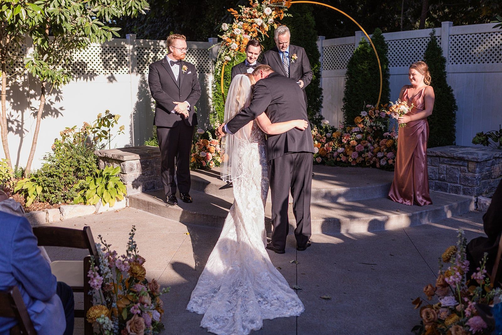 Caitlin hugs her dad at the floral arch at the end of the aisle as Gunnar looks on