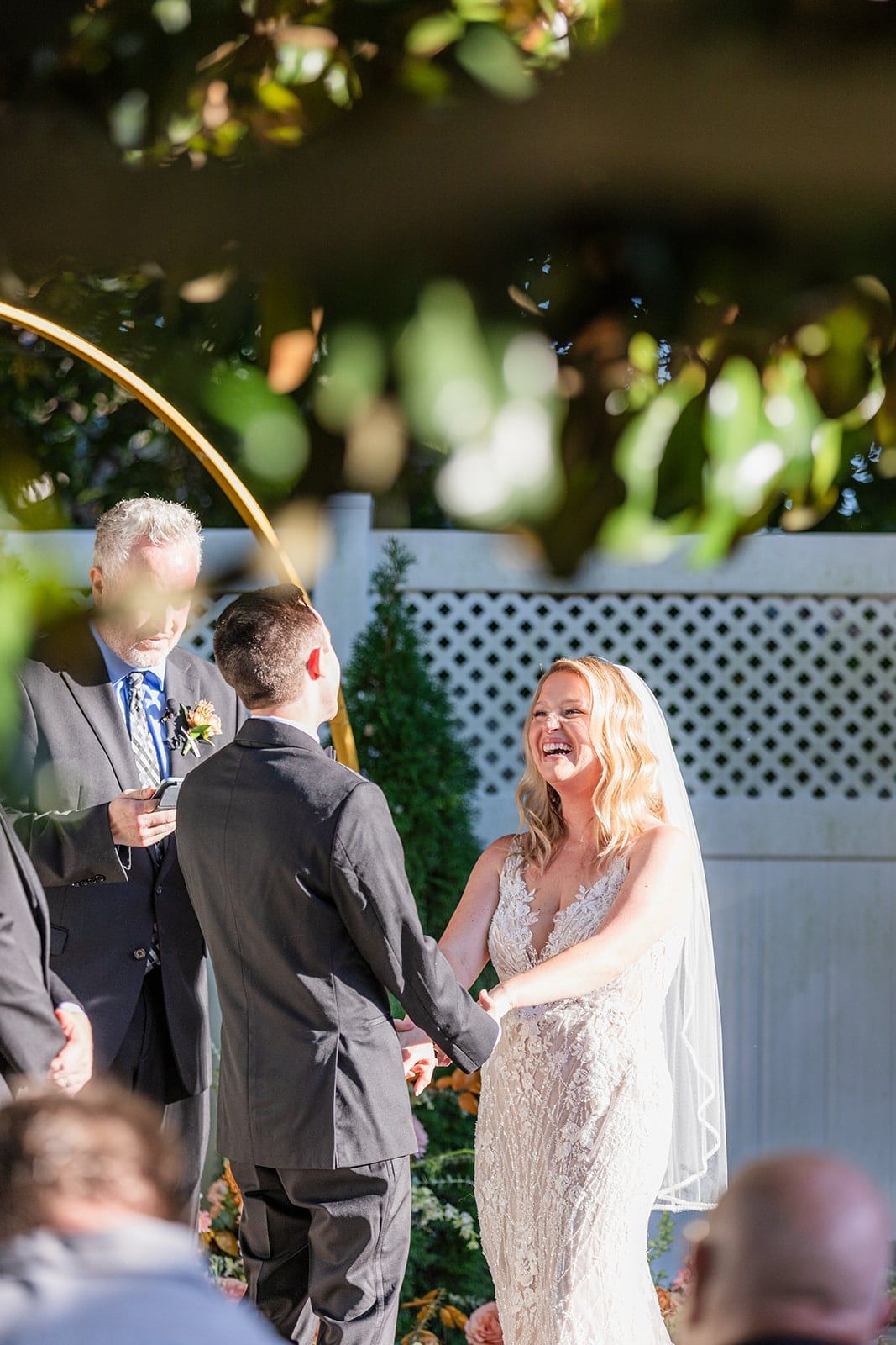 Caitlin laughs during the ceremony, framed through the leaves