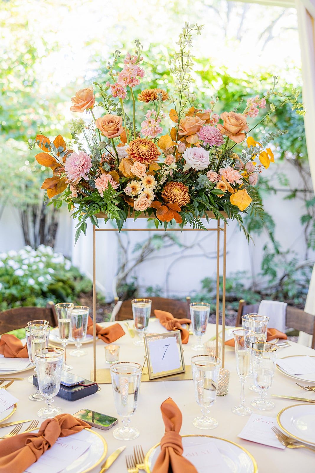 A tall centerpiece of peach and orange flowers above a set reception table