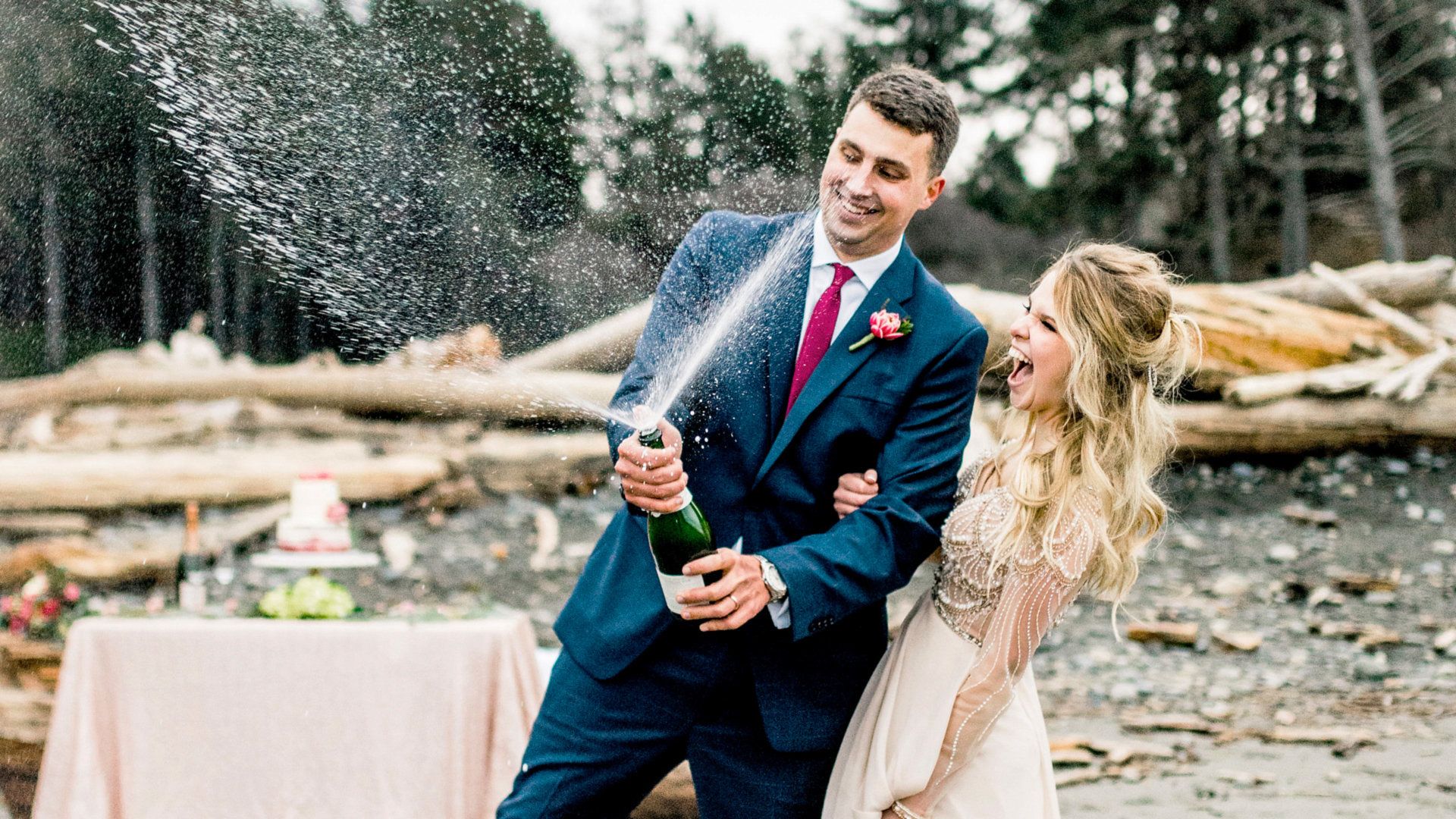 Danielle and Brandon pop champagne on Ruby Beach after their elopement, the spray arcing through the air