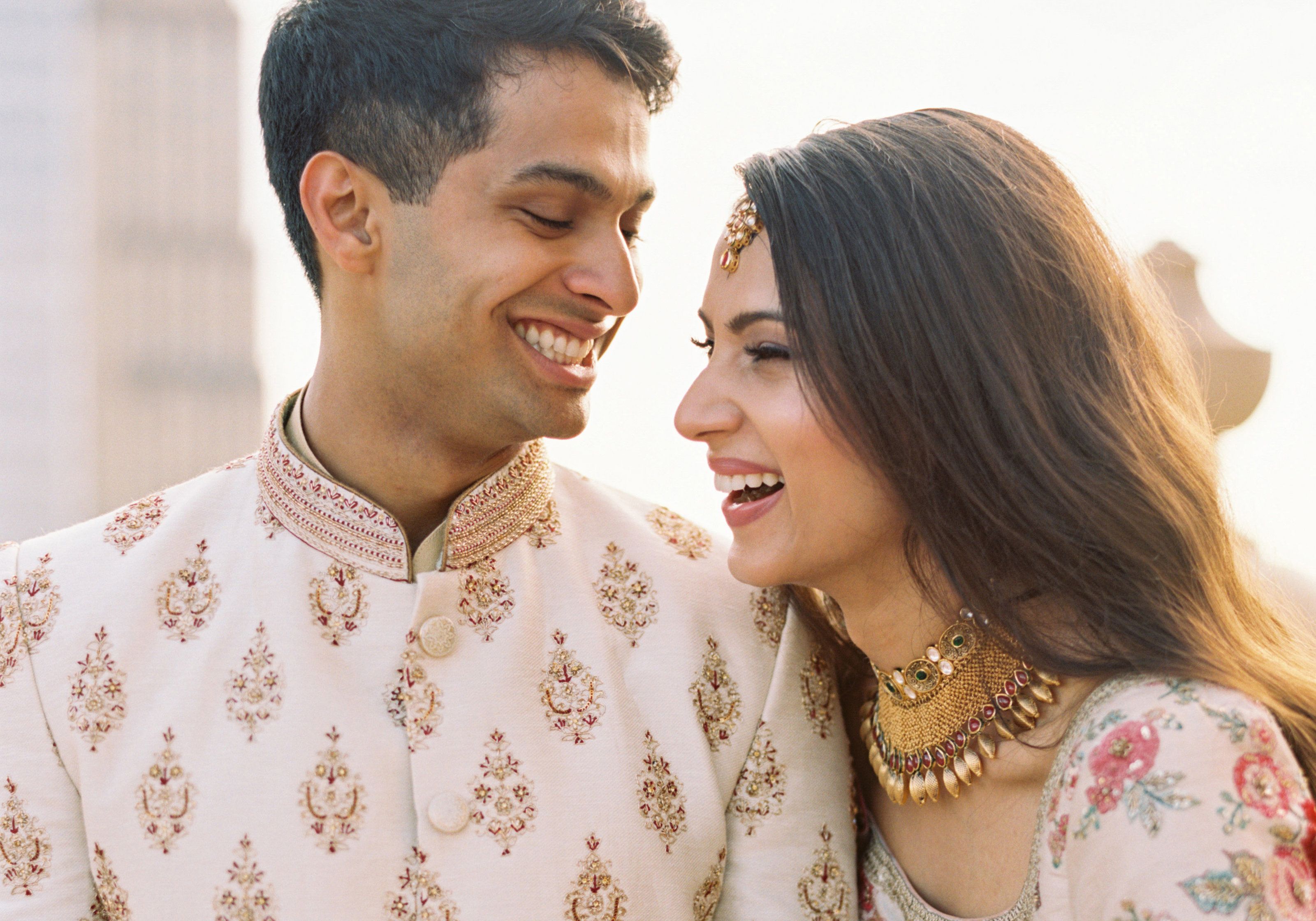 Nayha and Zubin laugh together in embroidered Indian wedding attire, foreheads almost touching