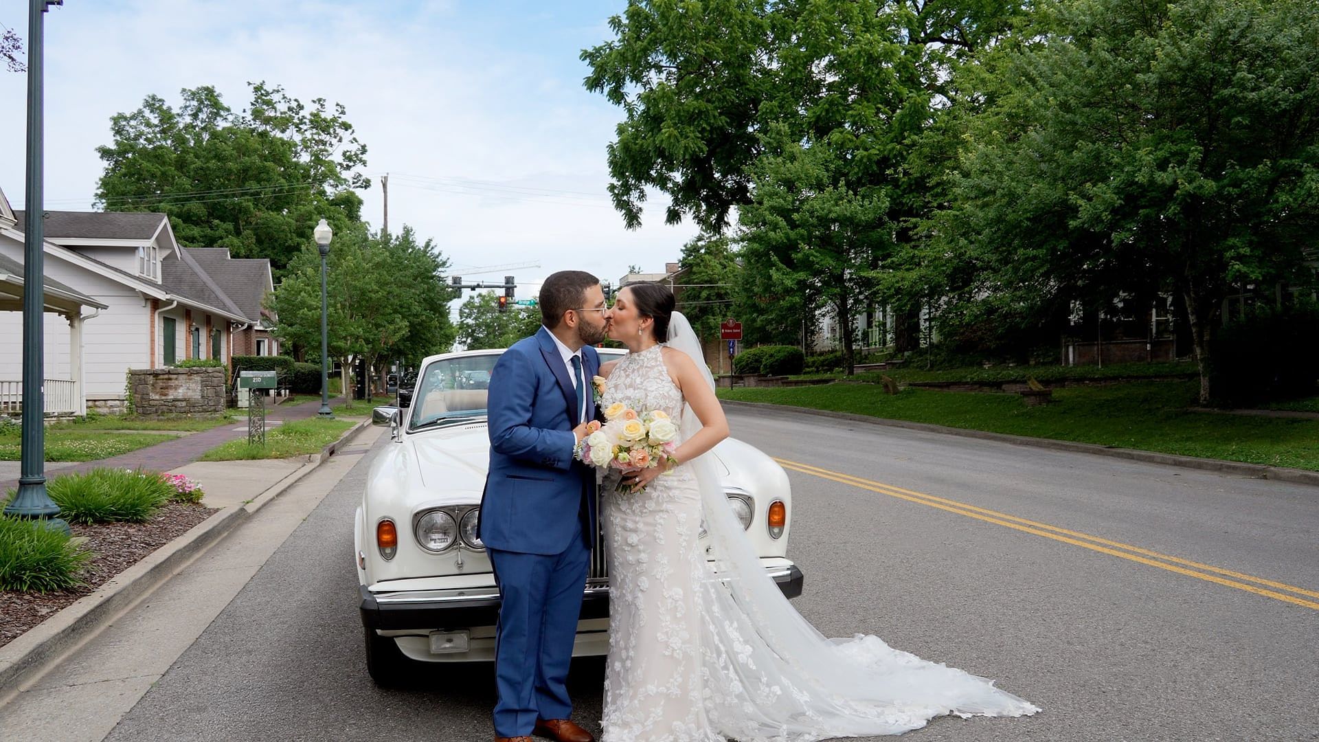 Andreina and Eric kiss beside a vintage white Rolls-Royce on a tree-lined street in Franklin
