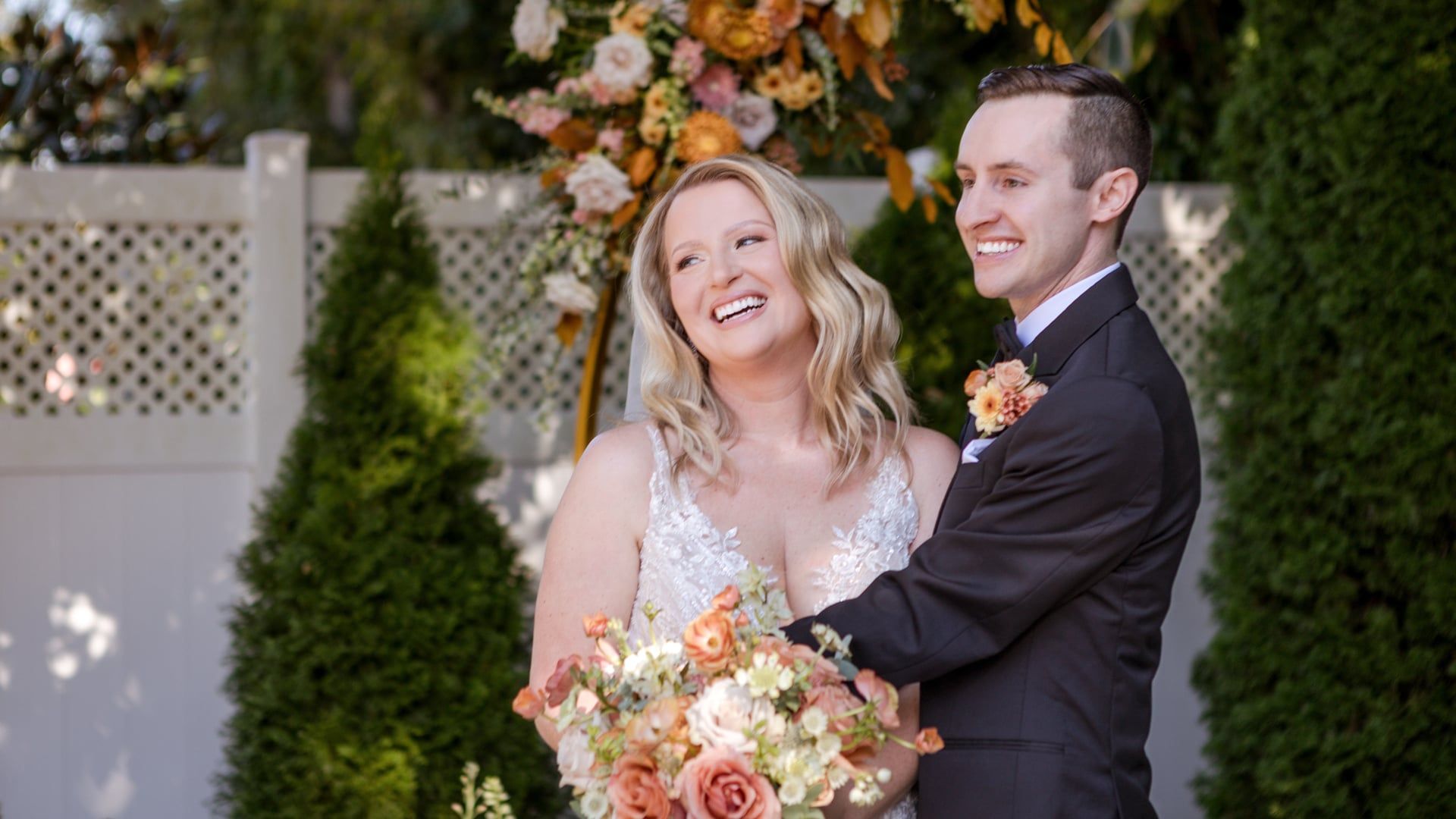 Caitlin laughs and looks up at Gunnar in front of a floral arch in the garden at CJ's Off the Square