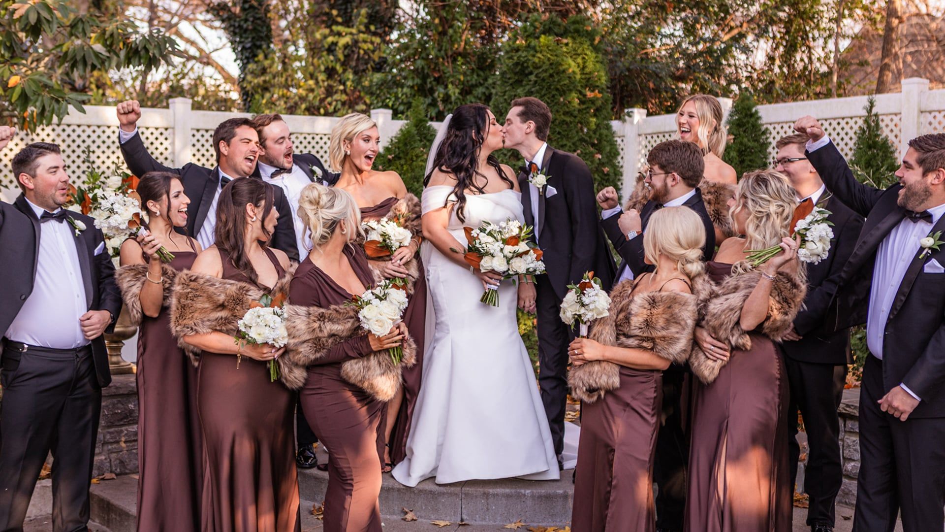 Caroline and Justin kiss as their wedding party cheers around them in the garden at CJ's Off the Square