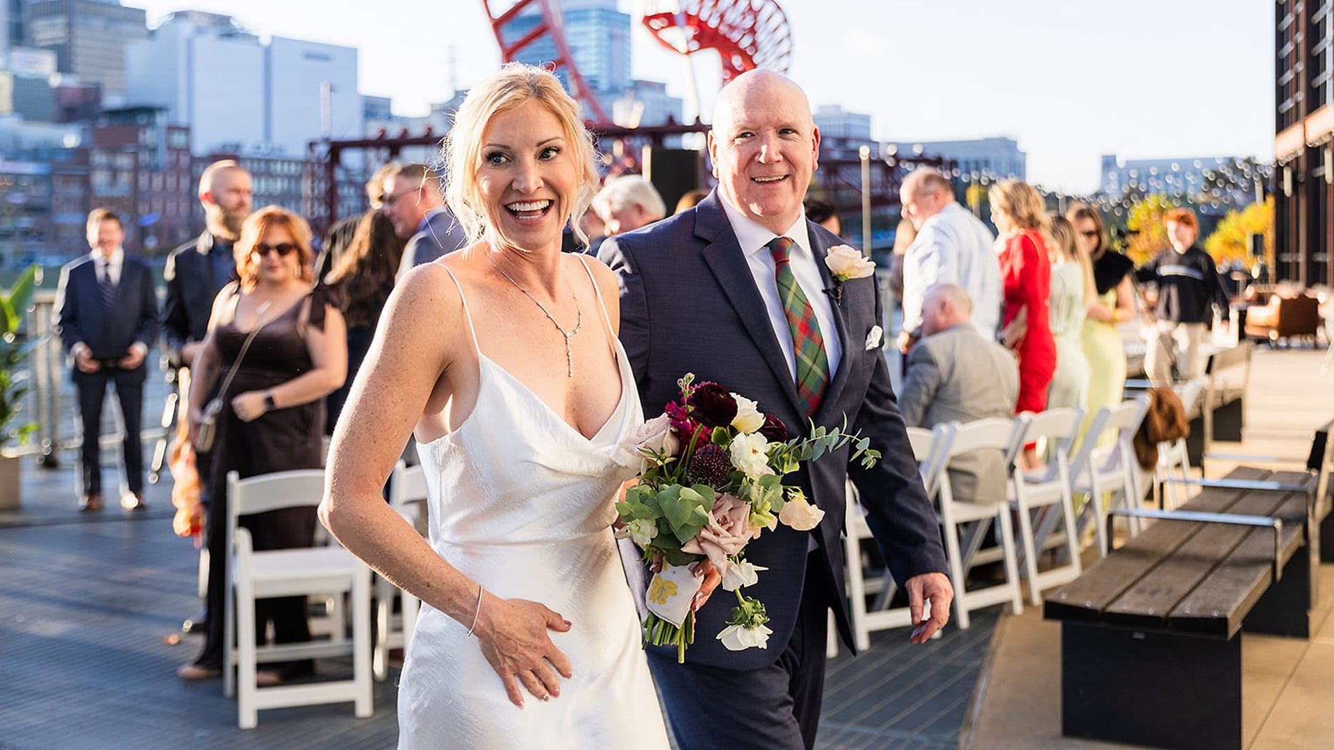 Casey and Mark walk down the aisle together, laughing, as guests look on at The Bridge Building, with the Nashville skyline behind them