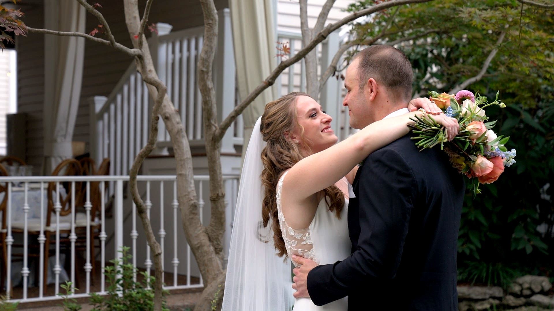 Emily wraps her arms around John's neck, bouquet in hand, in the garden at CJ's Off the Square