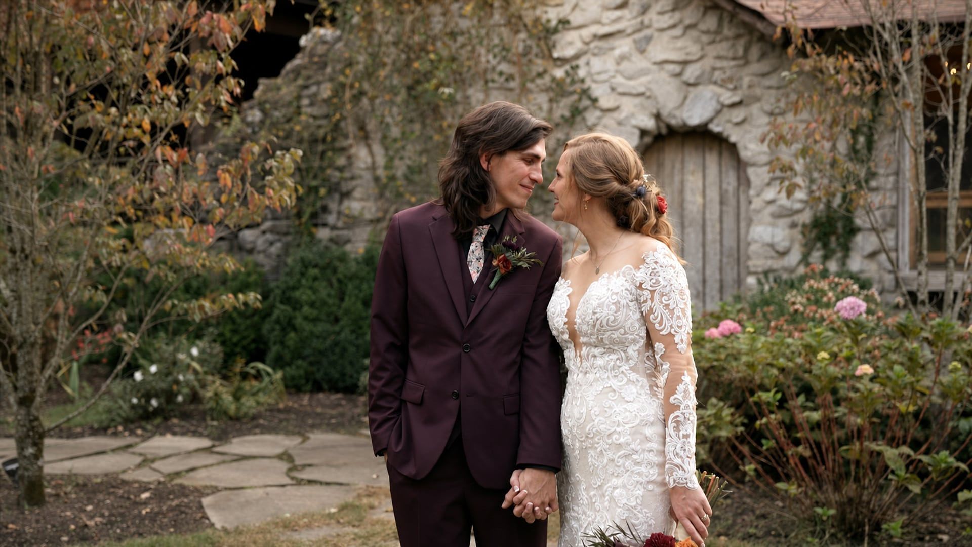 Kara and Jeremy hold hands and smile at each other in front of the stone buildings at Ruskin Cave