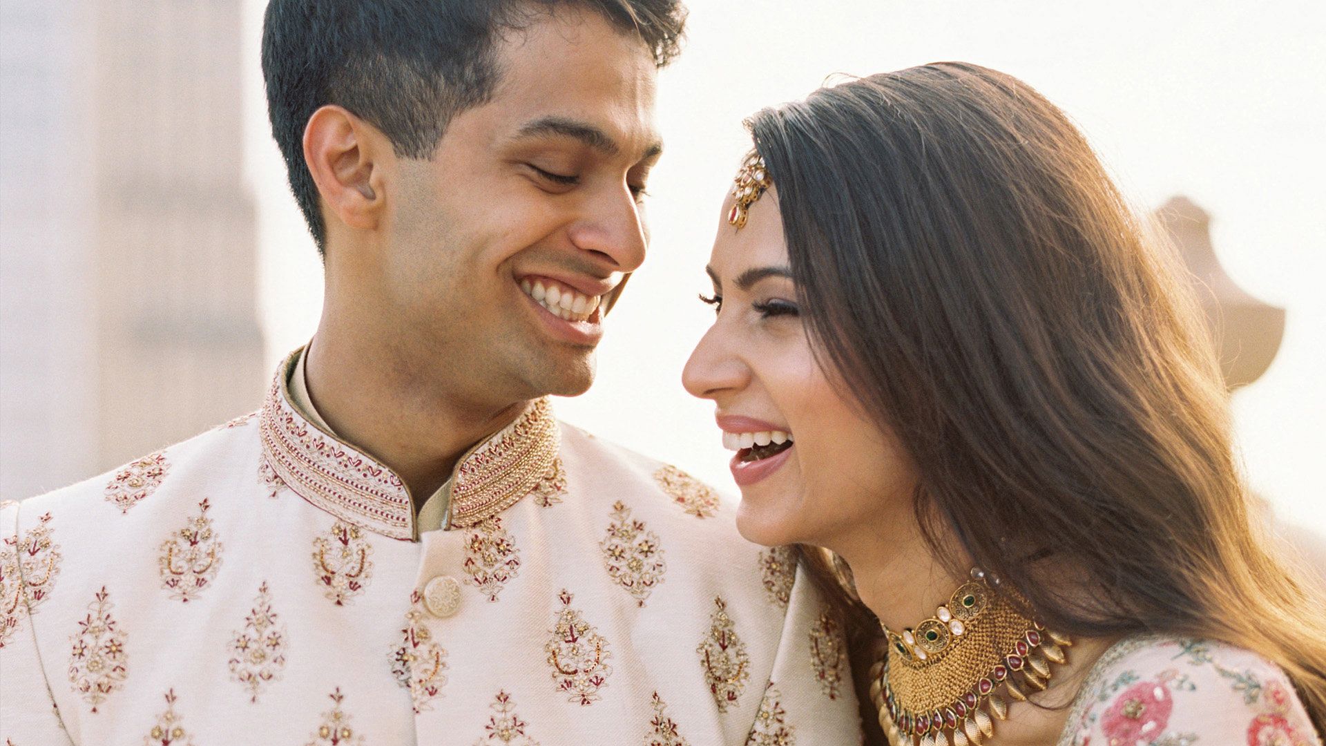 Nayha and Zubin laugh together in embroidered Indian wedding attire, foreheads almost touching