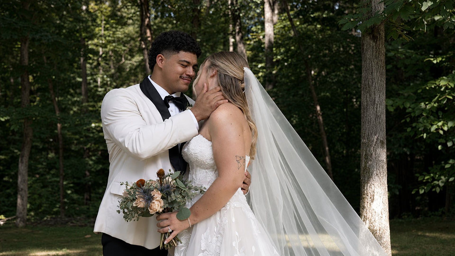 Olivia holds Lloyd's face as they share a quiet moment in the woods, her veil trailing behind her