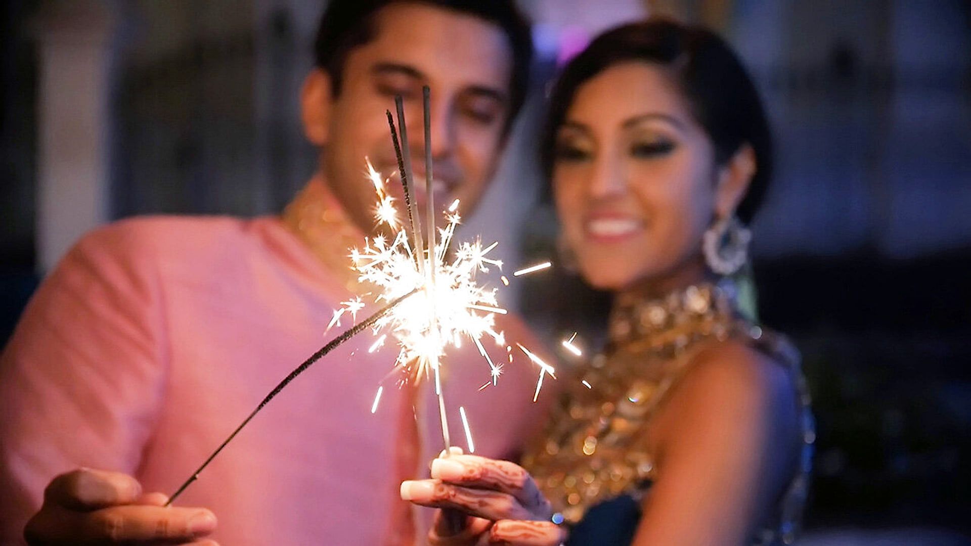 Serena and Ajay smile behind a lit sparkler at their sangeet