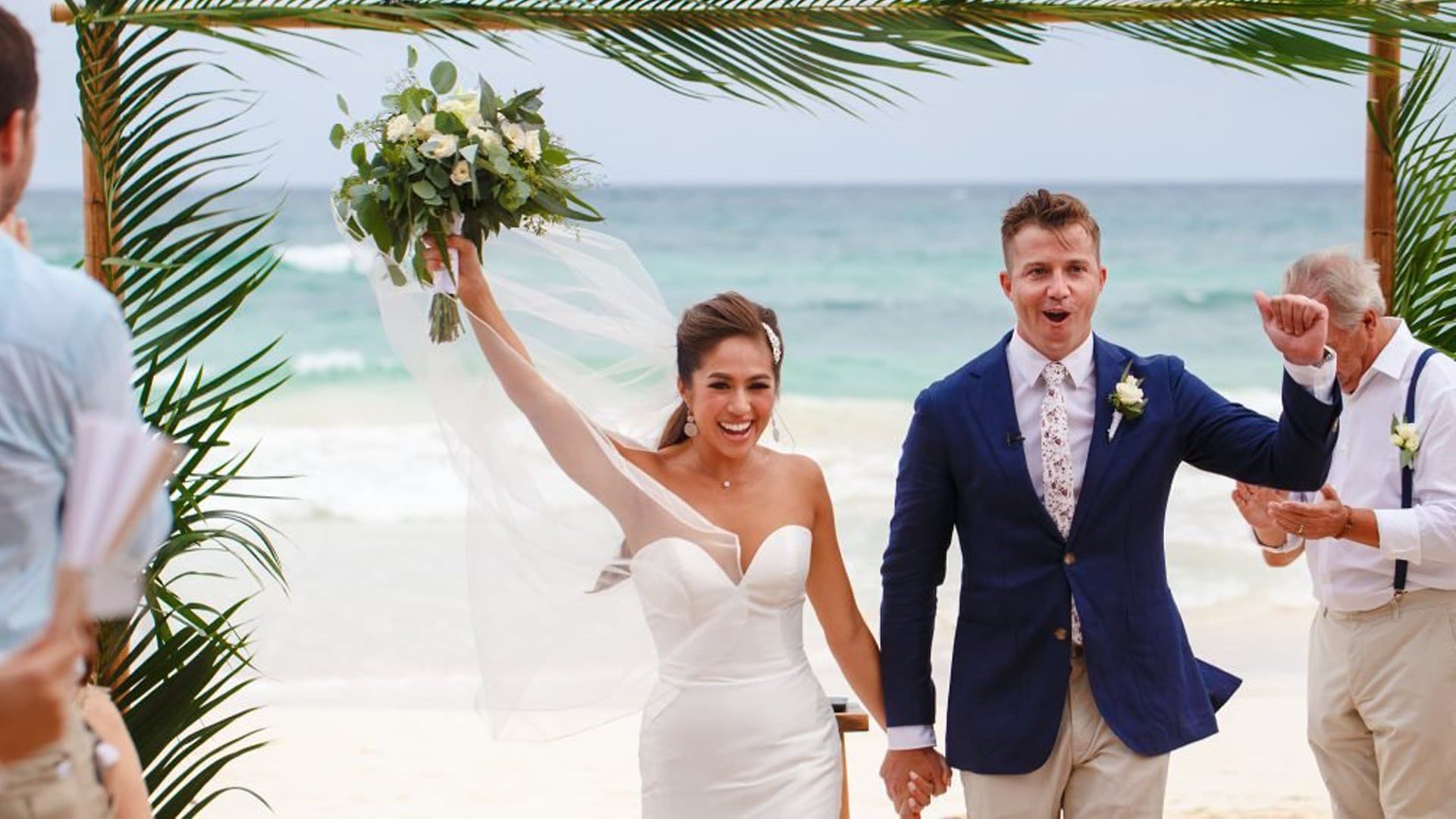 Tee raises her bouquet in celebration as she and Chris head back up the aisle on a Tulum beach