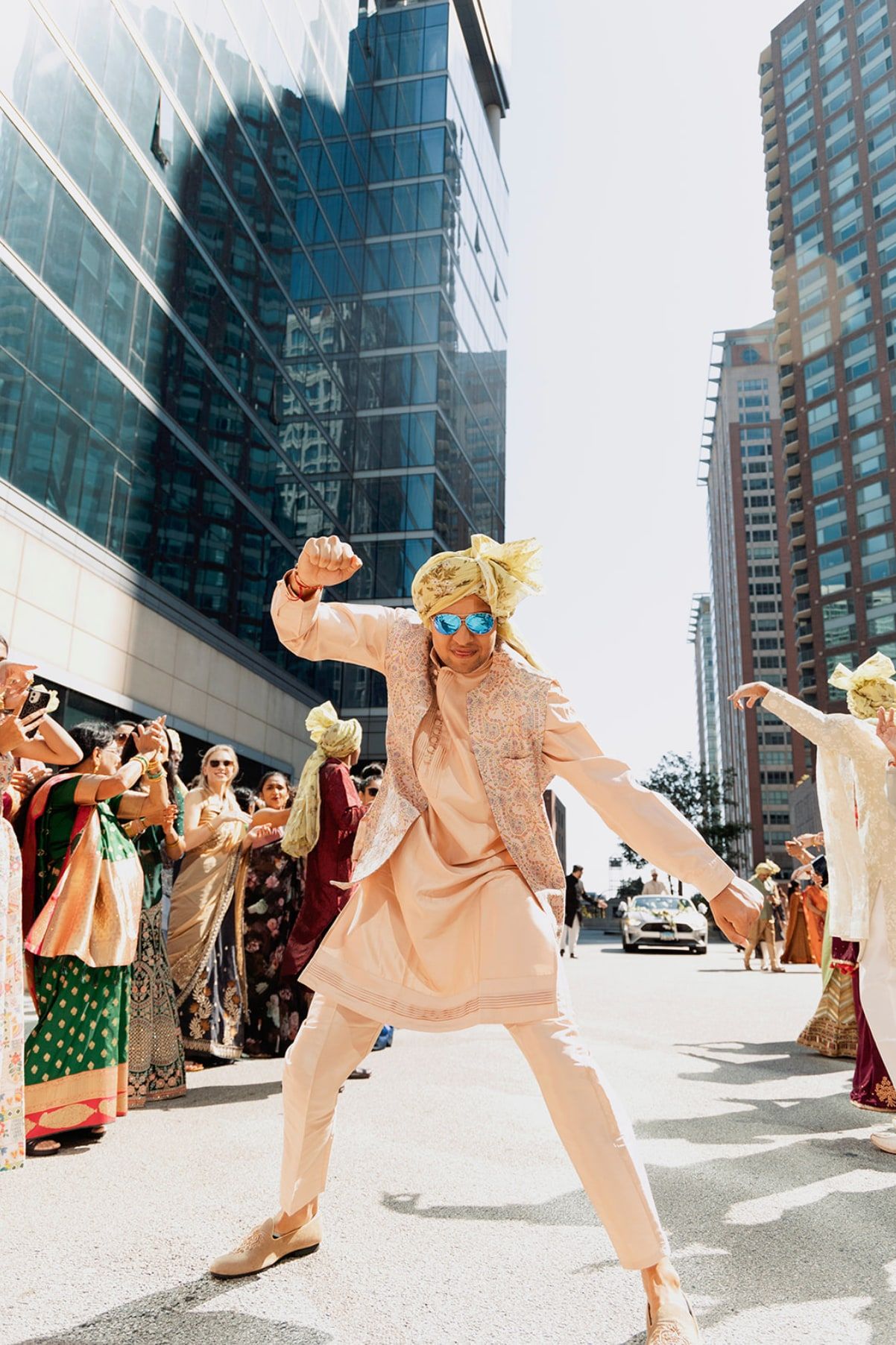 Groomsman in blue sunglasses and a gold turban dancing in the street during the baraat
