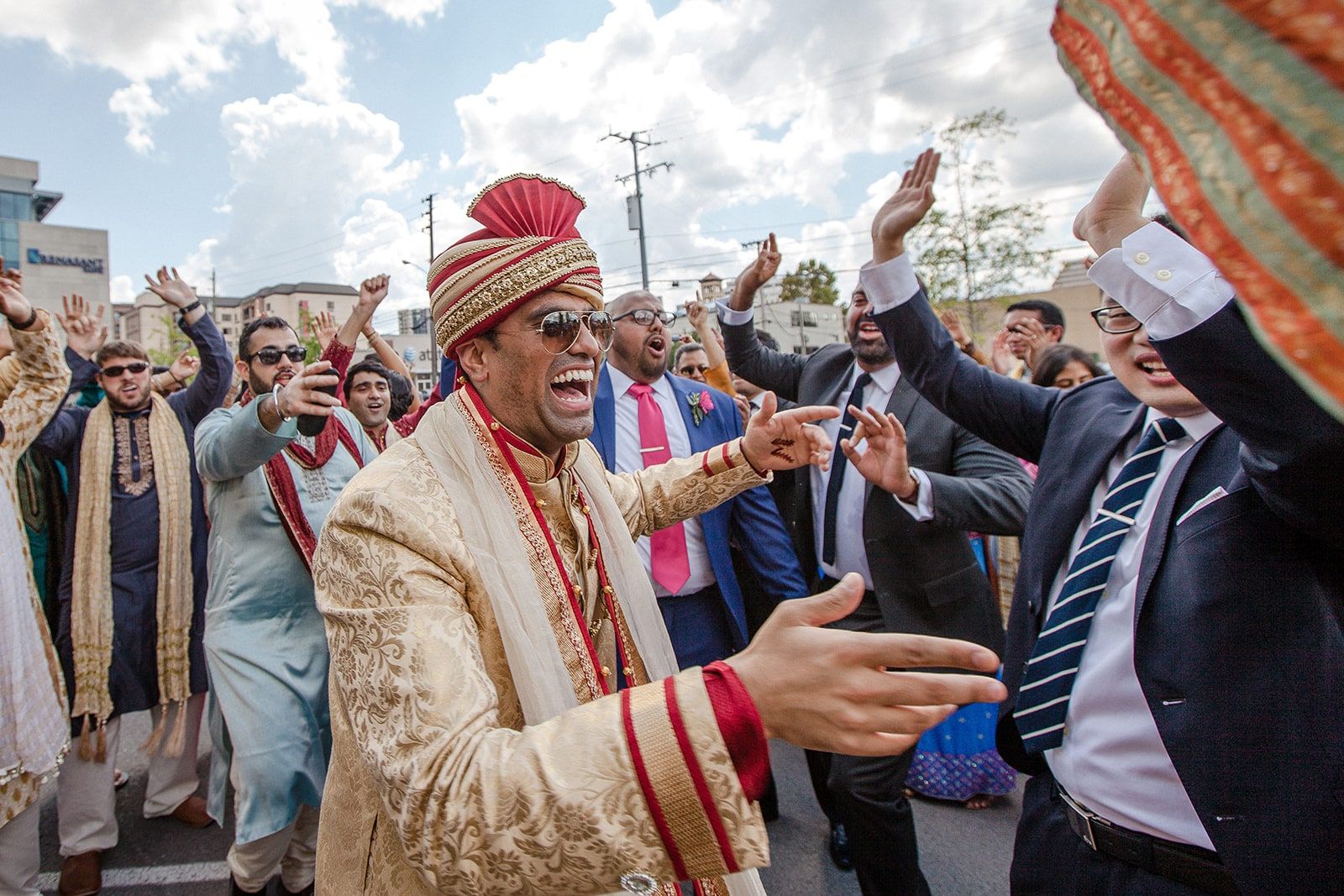 Groomsman in a gold sherwani and turban dancing in the baraat, surrounded by cheering guests
