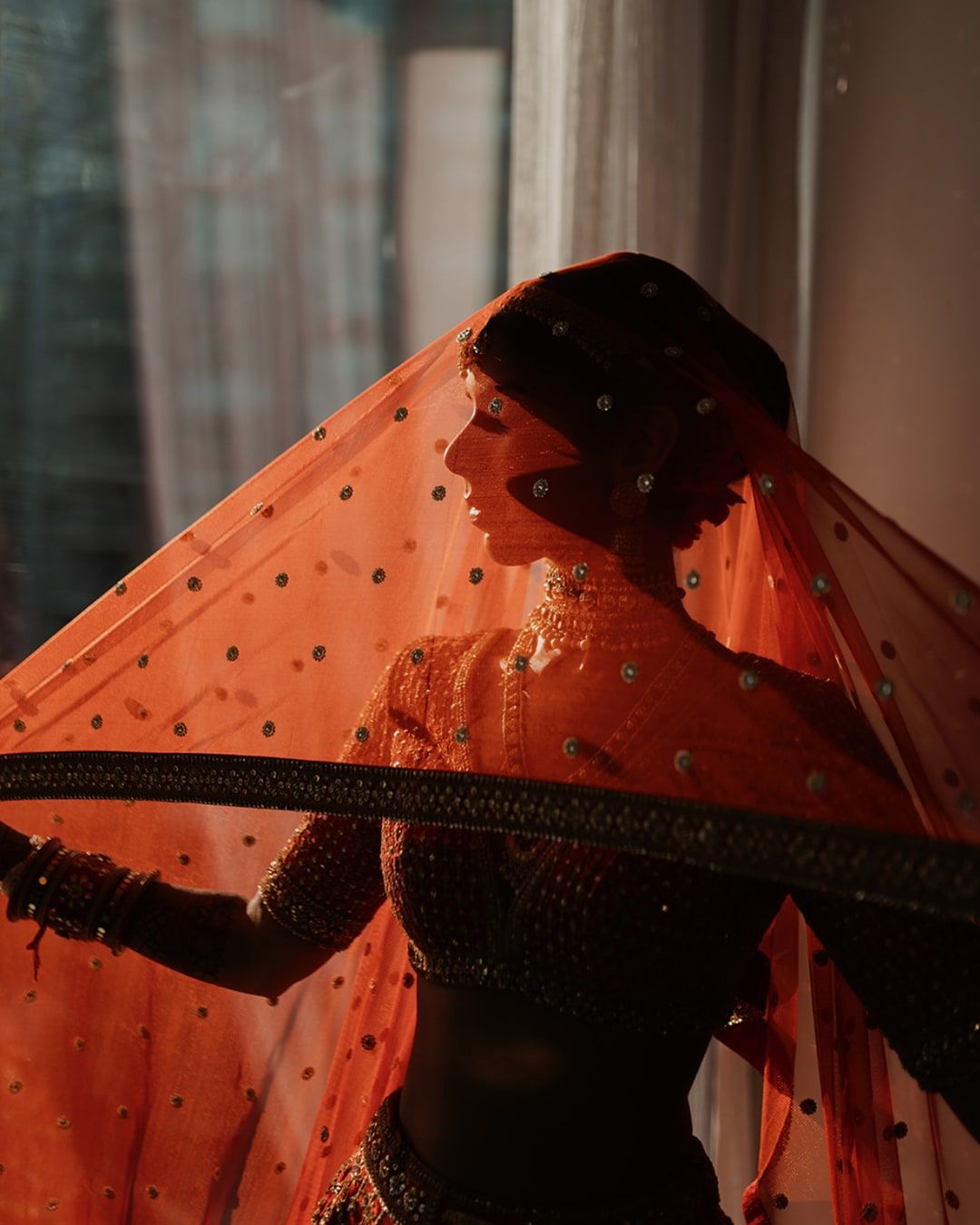 Bride in a red lehenga, window light falling through her sheer red dupatta