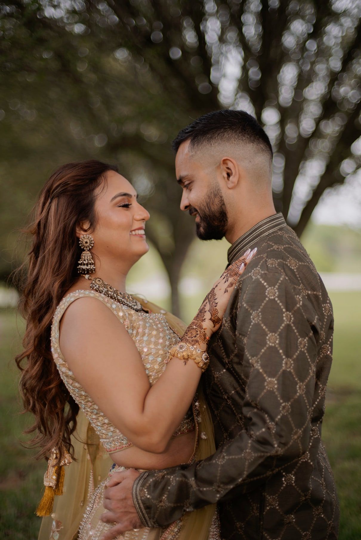 Couple embracing under the trees, her mehndi hand resting on his shoulder
