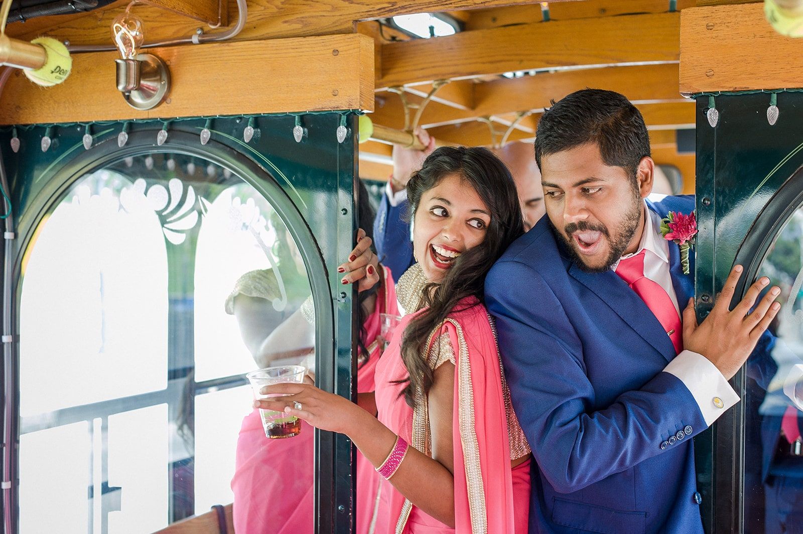 Couple hamming it up on a trolley, her in a pink sari with a drink, him in a blue suit