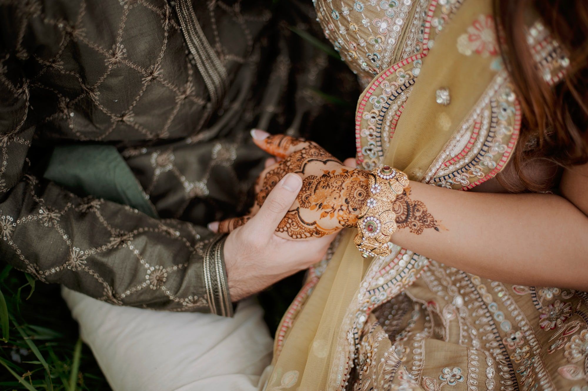 Groom holding the bride’s mehndi hand, gold jewelry at her wrist