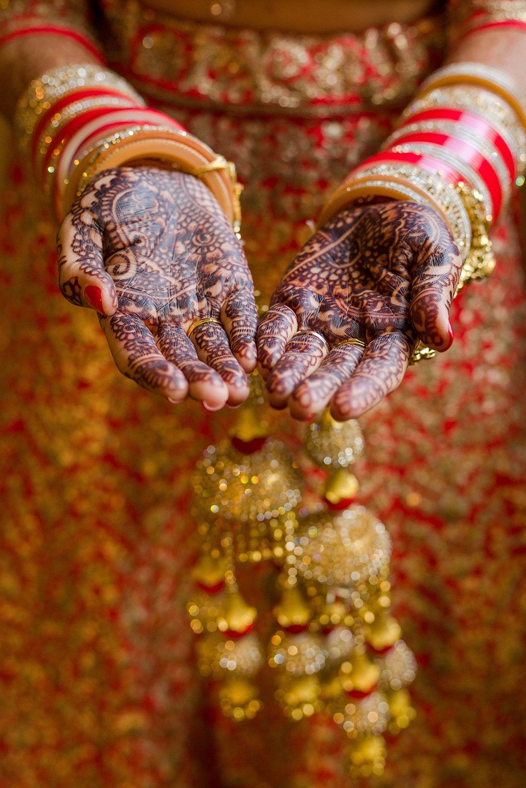 Bride’s cupped mehndi hands above gold kaleere, red and white bangles at her wrists