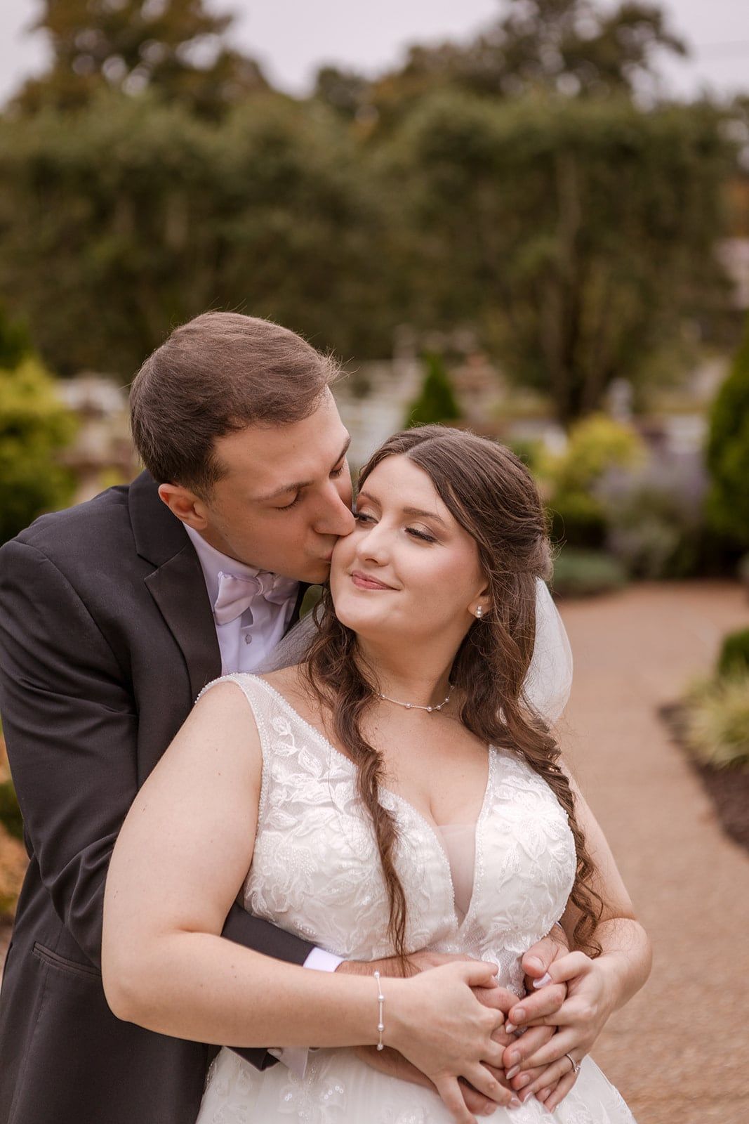Arms wrapped around her from behind, a kiss on the temple in a garden