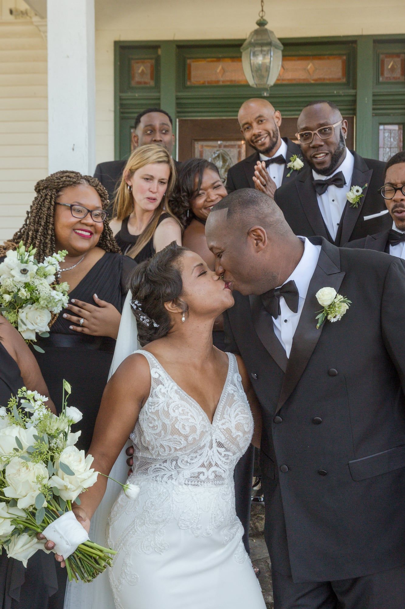 A couple kisses in a doorway while their wedding party cheers behind them