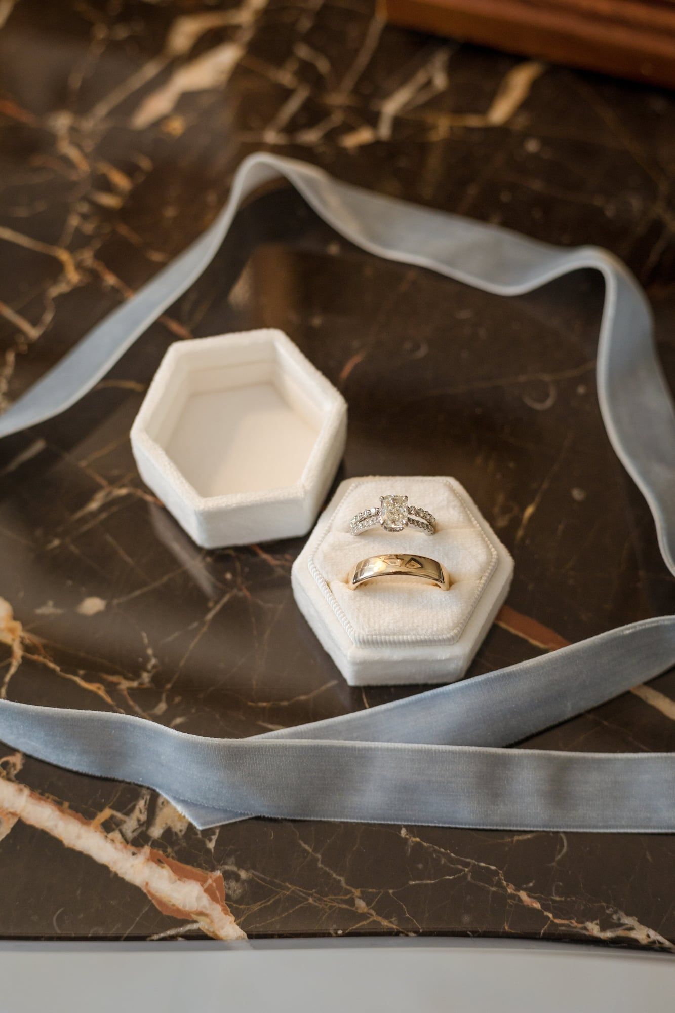 Wedding rings in a white box on dark marble, wrapped in a blue velvet ribbon