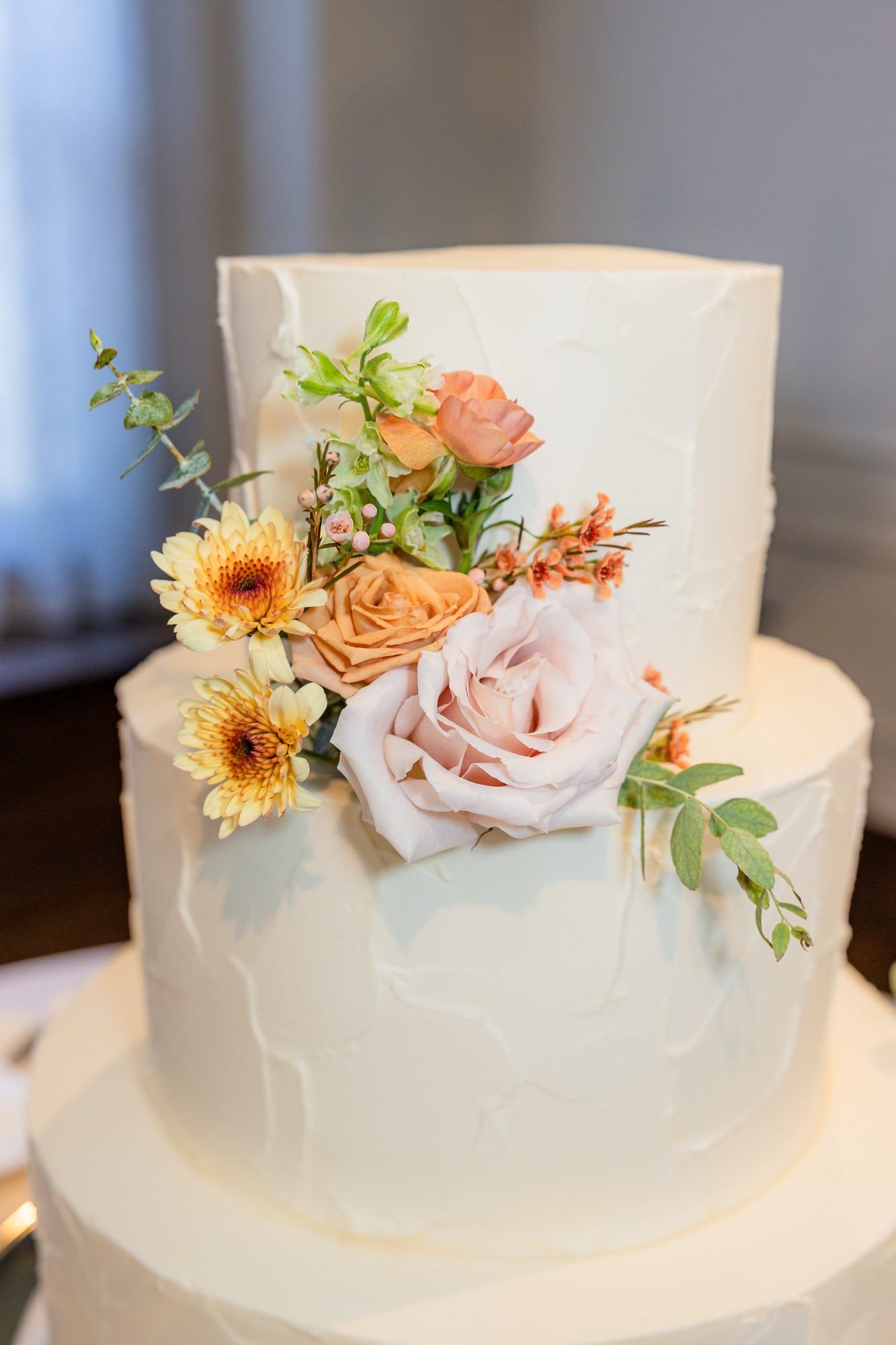A white two-tier wedding cake topped with orange, peach and yellow flowers