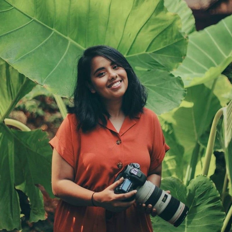 Tanya, our lead photographer for Indian weddings, smiling with her camera among giant green leaves