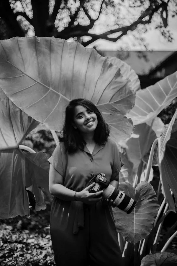 Tanya, our lead photographer for Indian weddings, smiling with her camera among giant green leaves