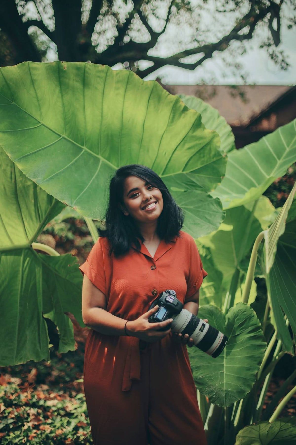 Tanya, our lead photographer for Indian weddings, smiling with her camera among giant green leaves