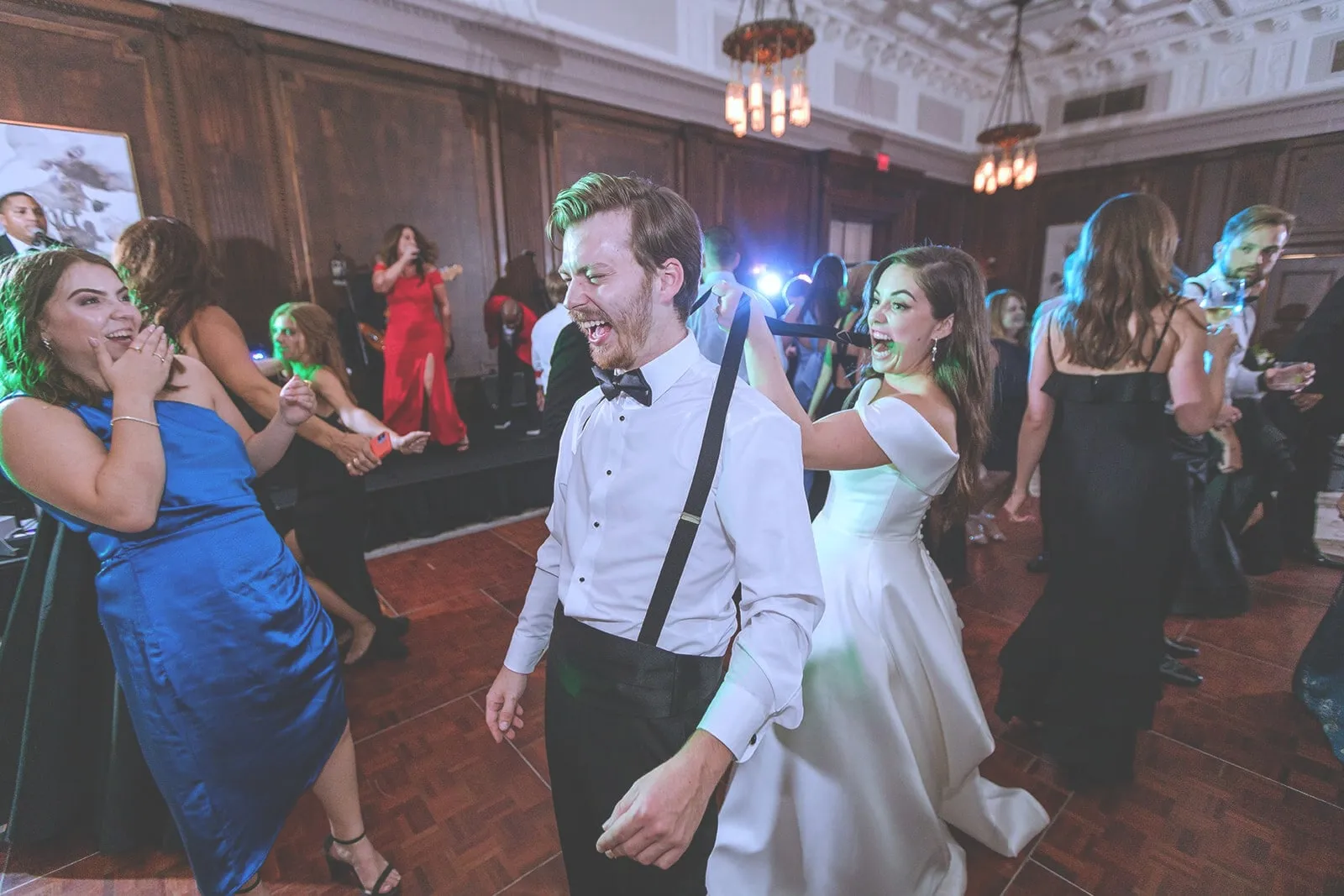 Guests laugh and dance around the couple in a wood-paneled ballroom