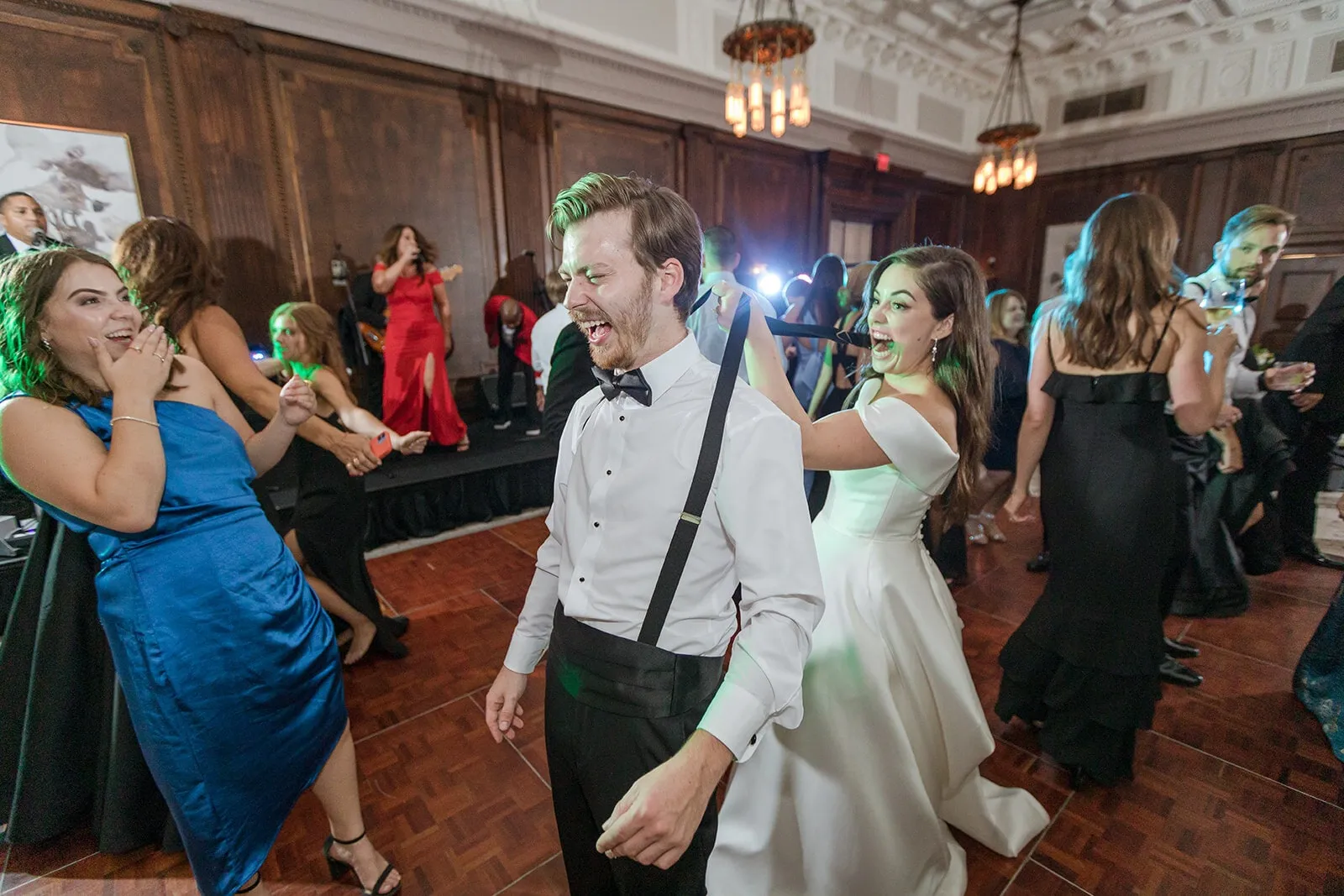 Guests laugh and dance around the couple in a wood-paneled ballroom
