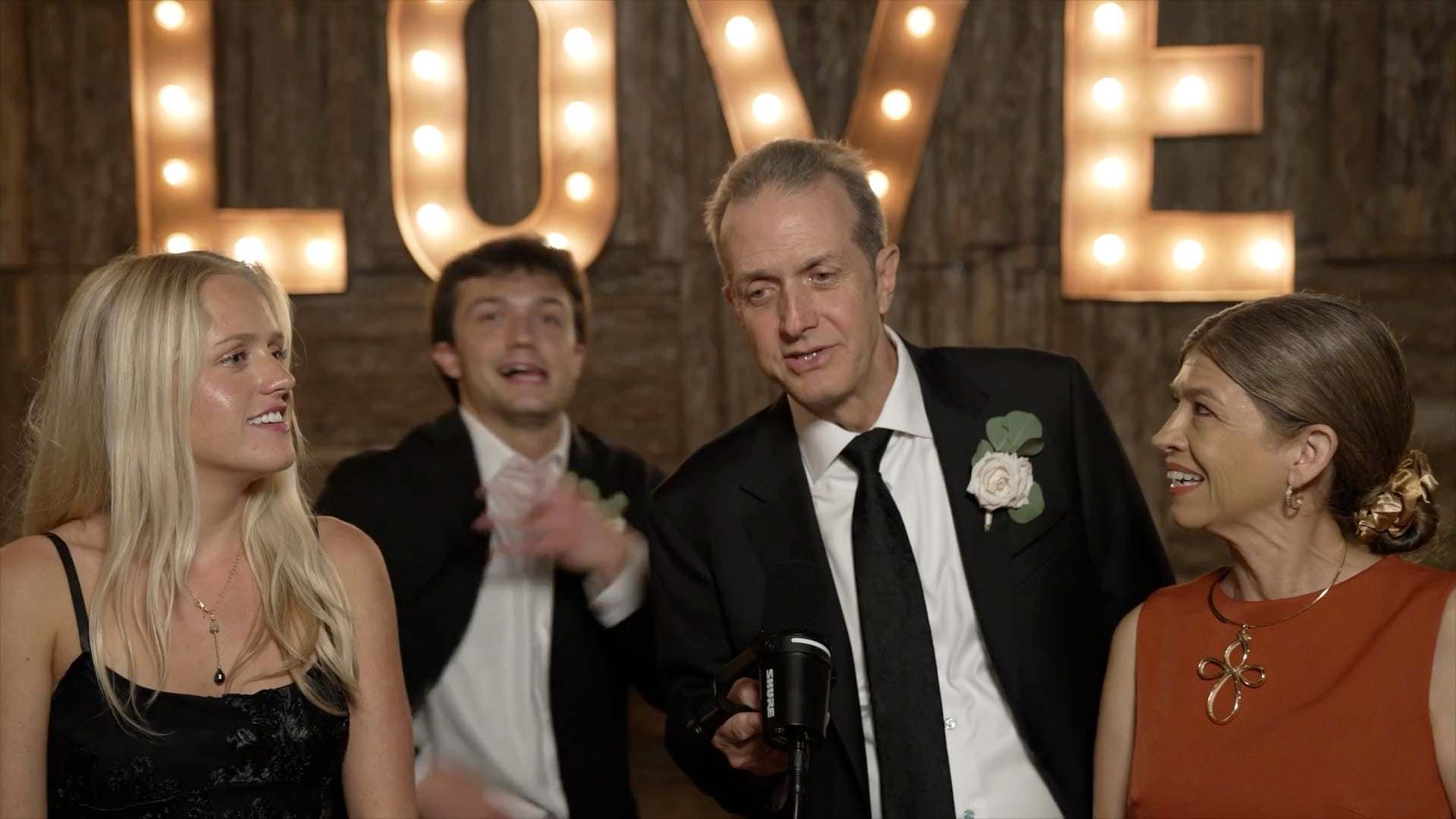 Wedding guests laughing together at the Unscripted booth mic under a lit LOVE marquee