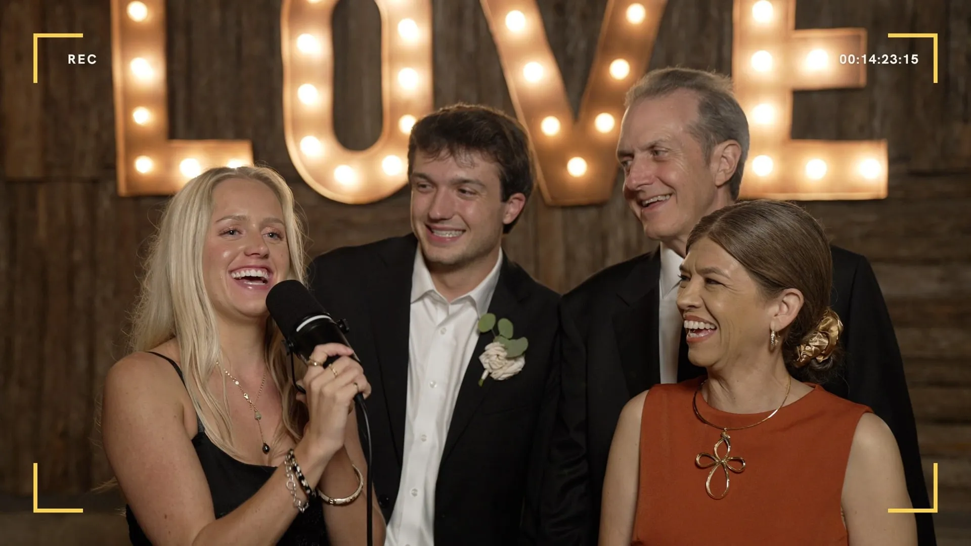 The groom's dad, brother, brother's girlfriend and stepmom laughing together at the Unscripted booth mic during Kenadee and Hampton's reception