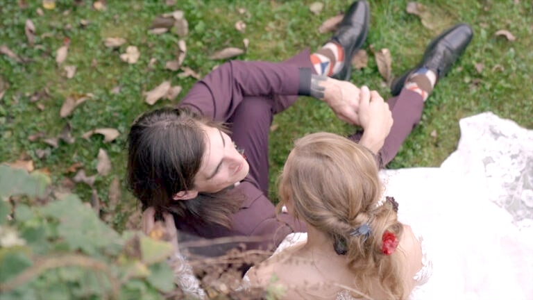Overhead view of bride and groom sharing a quiet moment on the grass at their fall wedding at Ruskin Cave in Dickson, TN. Filmed by With This Ring, Nashville wedding videographers, highlighting the bride’s lace dress and floral hair accessory.