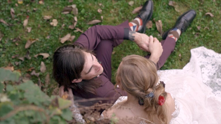 Overhead view of bride and groom sharing a quiet moment on the grass at their fall wedding at Ruskin Cave in Dickson, TN. Filmed by With This Ring, Nashville wedding videographers, highlighting the bride’s lace dress and floral hair accessory.