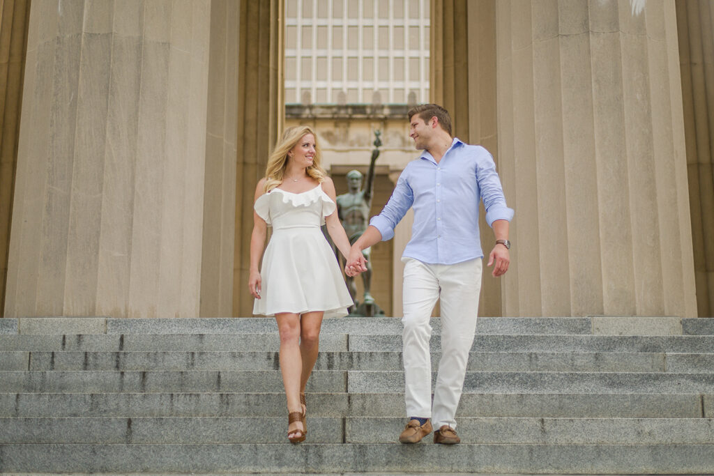 Bride Taylor and Groom Michael hold hands while walking down the steps at iconic Nashville engagement photo shoot location The Parthenon.